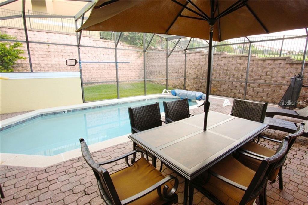 A patio features a dining set under an umbrella next to a screened-in swimming pool — 3152 YELLOW LANTANA LANE, KISSIMMEE, FL