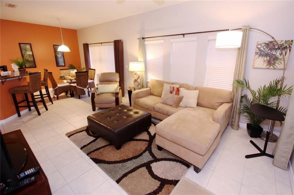 A living room with a beige sectional, leather ottoman, and an adjacent dining area — 3152 YELLOW LANTANA LANE, KISSIMMEE, FL