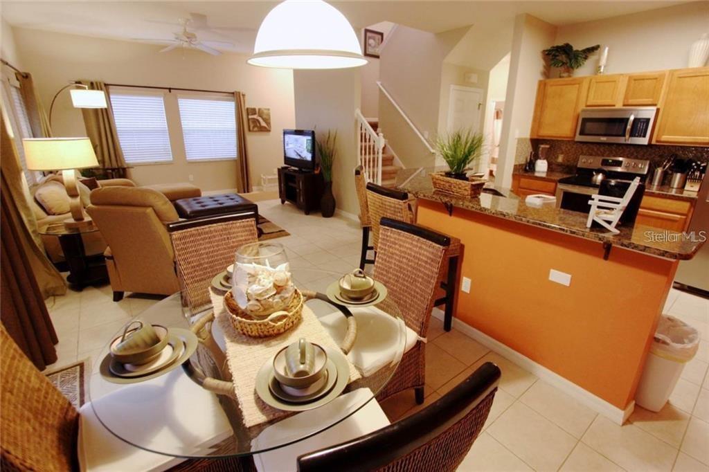 A dining area with a glass table sits in front of an open kitchen and living room — 3152 YELLOW LANTANA LANE, KISSIMMEE, FL