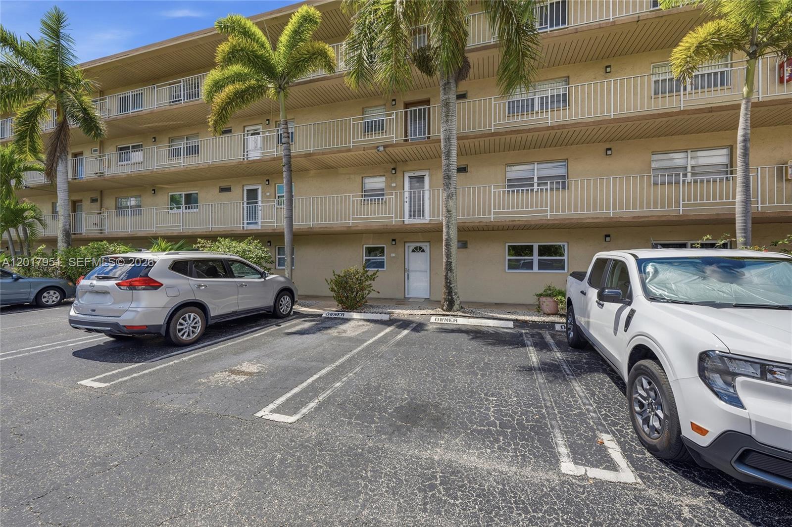 The exterior of a multi-story apartment building features balconies, palm trees, and a parking lot — 330 NE 26th Ave # 1120, Boynton Beach FL 33435, BOYNTON BEACH, FL
