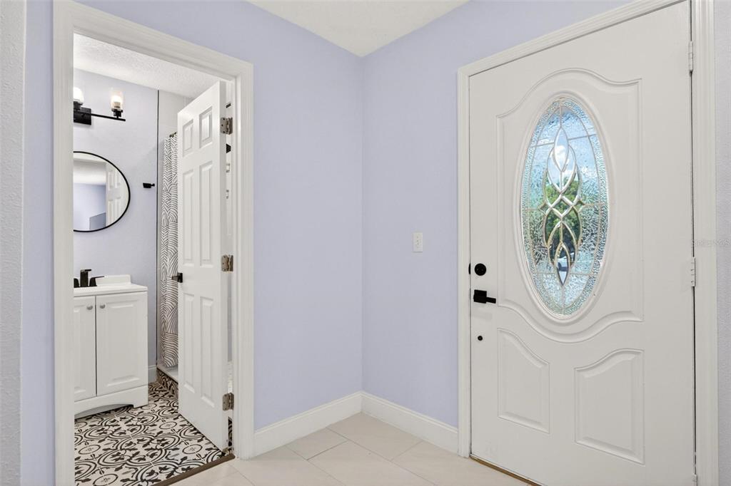 A white front door with a decorative glass oval sits beside a bathroom with patterned flooring — 700 S WELLINGTON DRIVE, DELTONA, FL