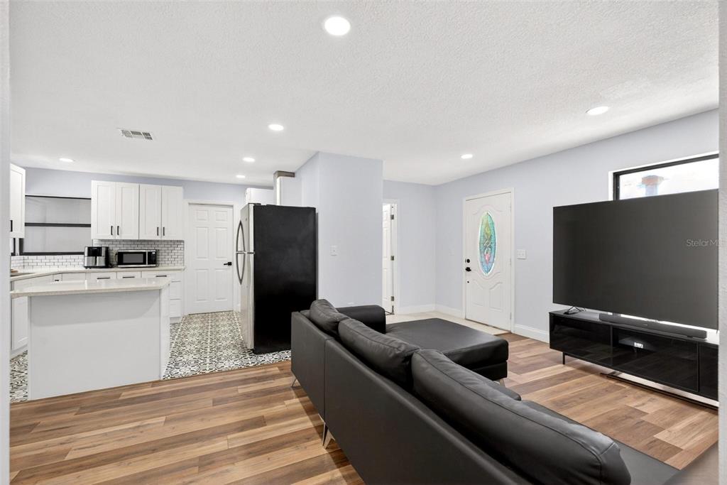 An open-concept living room and kitchen featuring wood-look flooring, a black sofa, and white cabinetry — 700 S WELLINGTON DRIVE, DELTONA, FL
