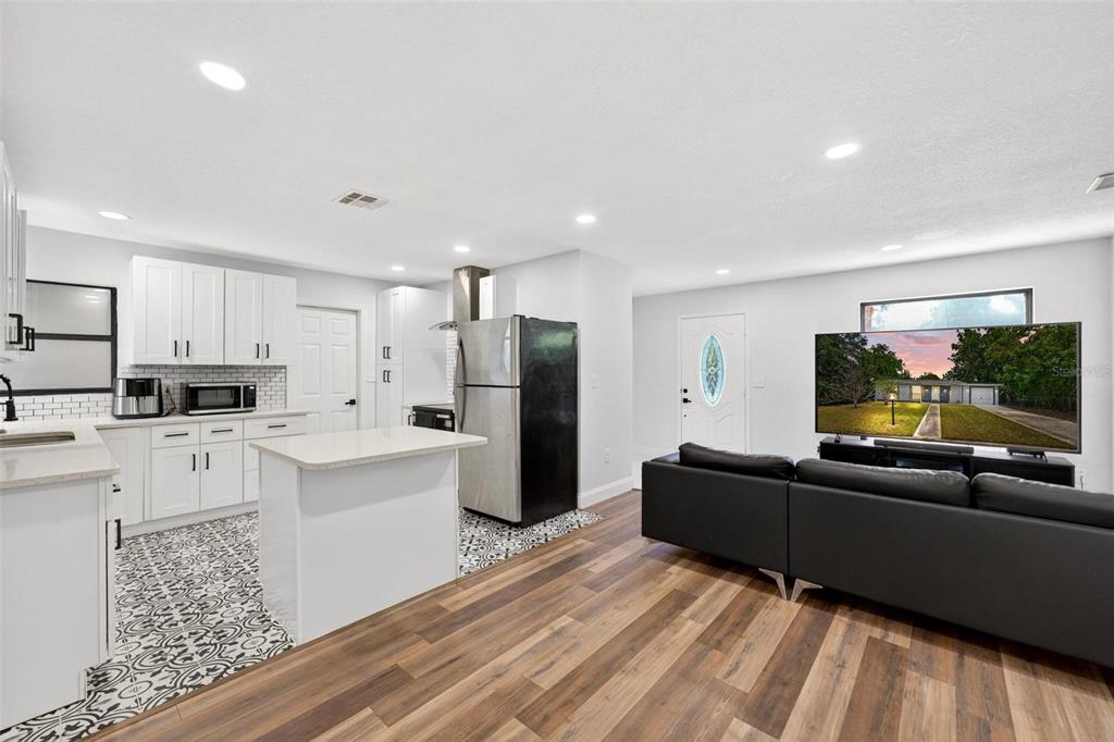 An open-concept kitchen and living area featuring white cabinets, patterned tile floors, and wood flooring — 700 S WELLINGTON DRIVE, DELTONA, FL