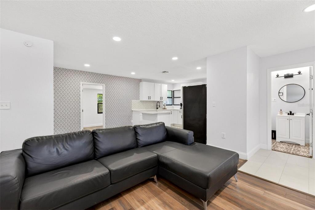 A living room features a black sectional sofa, wood-look flooring, and an adjacent open kitchen — 700 S WELLINGTON DRIVE, DELTONA, FL