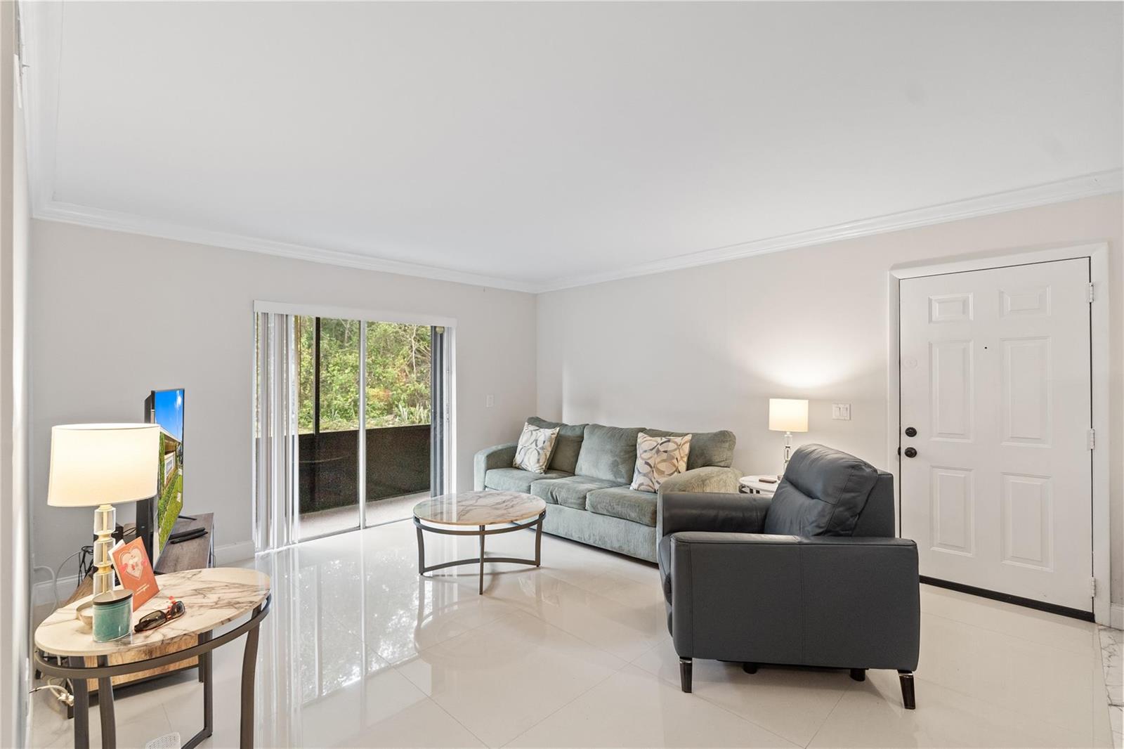 A living room features white tile flooring, a green sofa, a dark armchair, and sliding doors — 567 Trace Circle # 104, Deerfield Beach FL 33441, DEERFIELD BEACH, FL