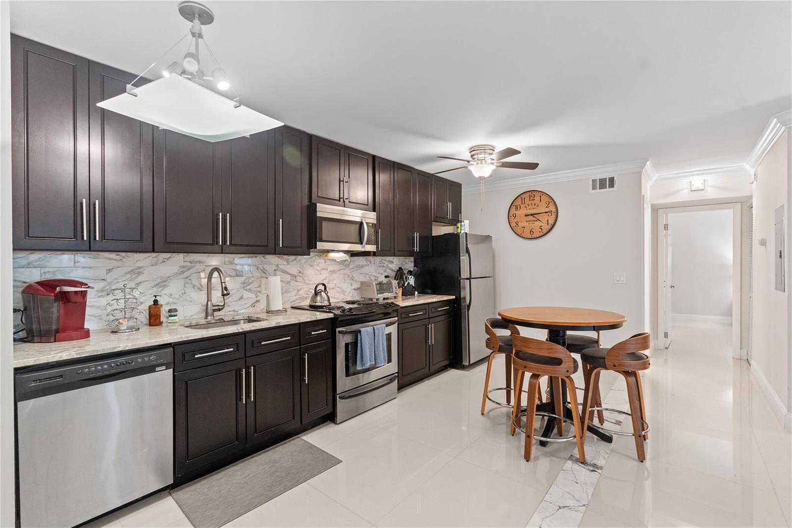 A modern kitchen features dark wood cabinets, stainless steel appliances, and a round dining table — 567 Trace Circle # 104, Deerfield Beach FL 33441, DEERFIELD BEACH, FL