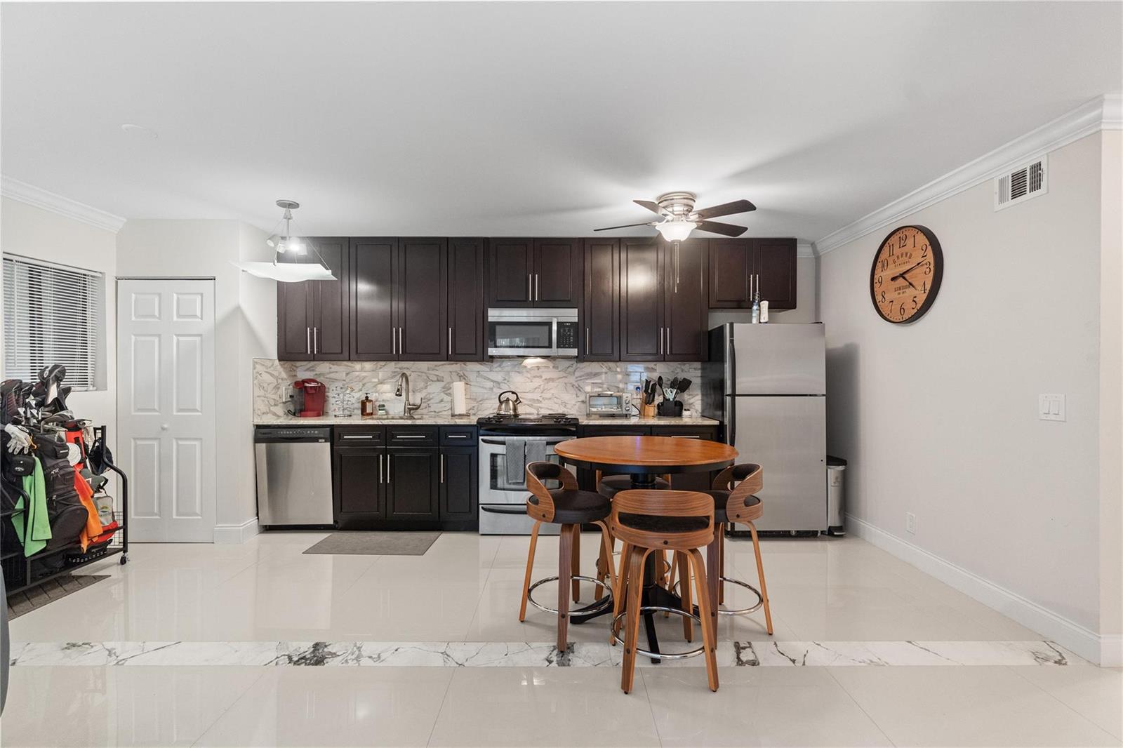 A kitchen features dark wood cabinets, stainless steel appliances, a marble backsplash, and a dining set — 567 Trace Circle # 104, Deerfield Beach FL 33441, DEERFIELD BEACH, FL