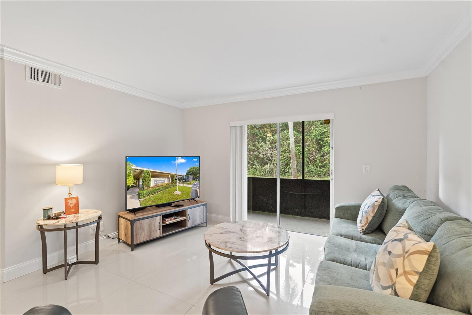 A living room features light tile floors, a sofa, a television, and a sliding glass door — 567 Trace Circle # 104, Deerfield Beach FL 33441, DEERFIELD BEACH, FL