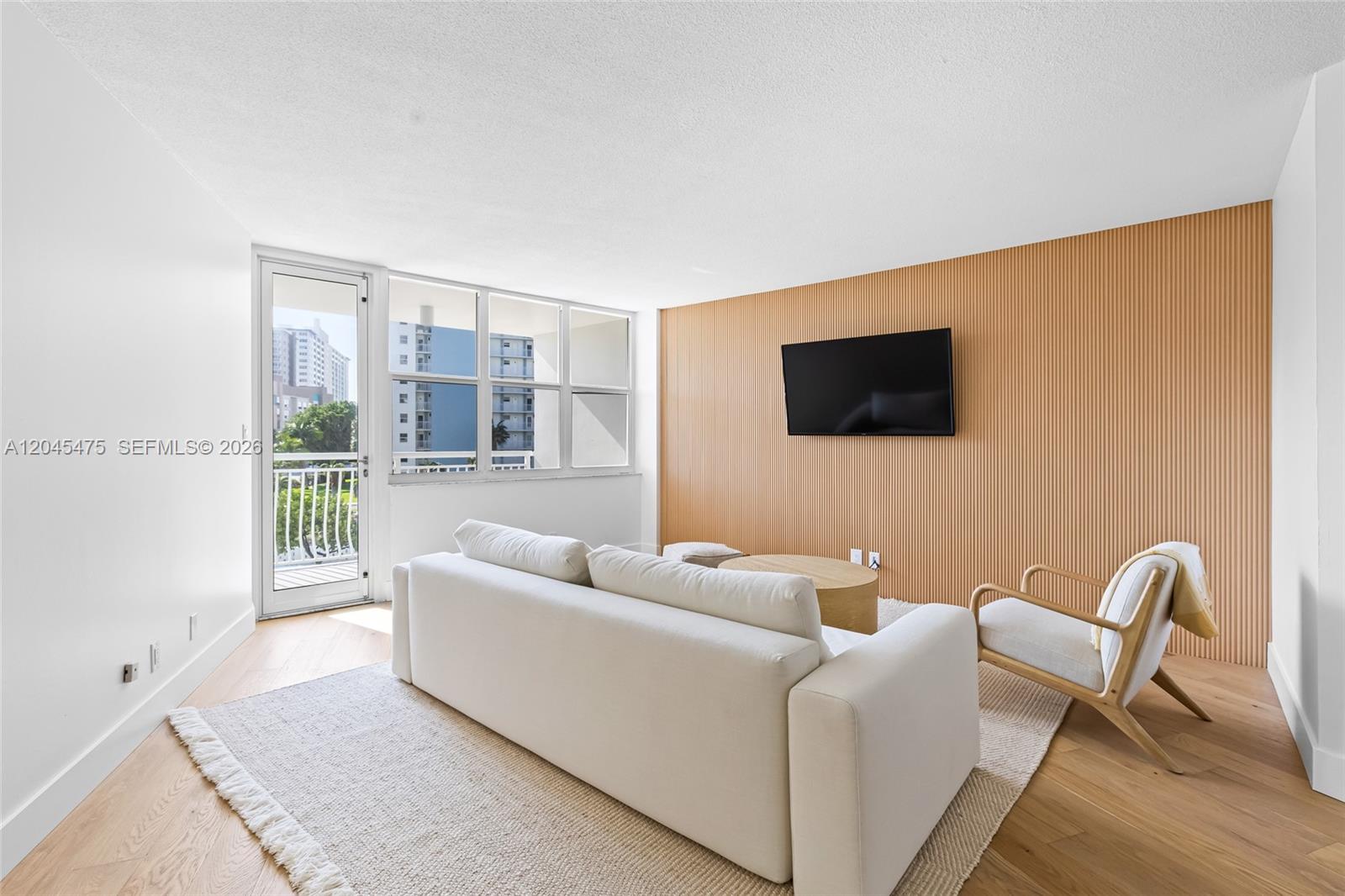 A living room features a white sofa, a slatted wood accent wall, and a balcony door — 301 N Ocean Blvd # 302, Pompano Beach FL 33062, POMPANO BEACH, FL