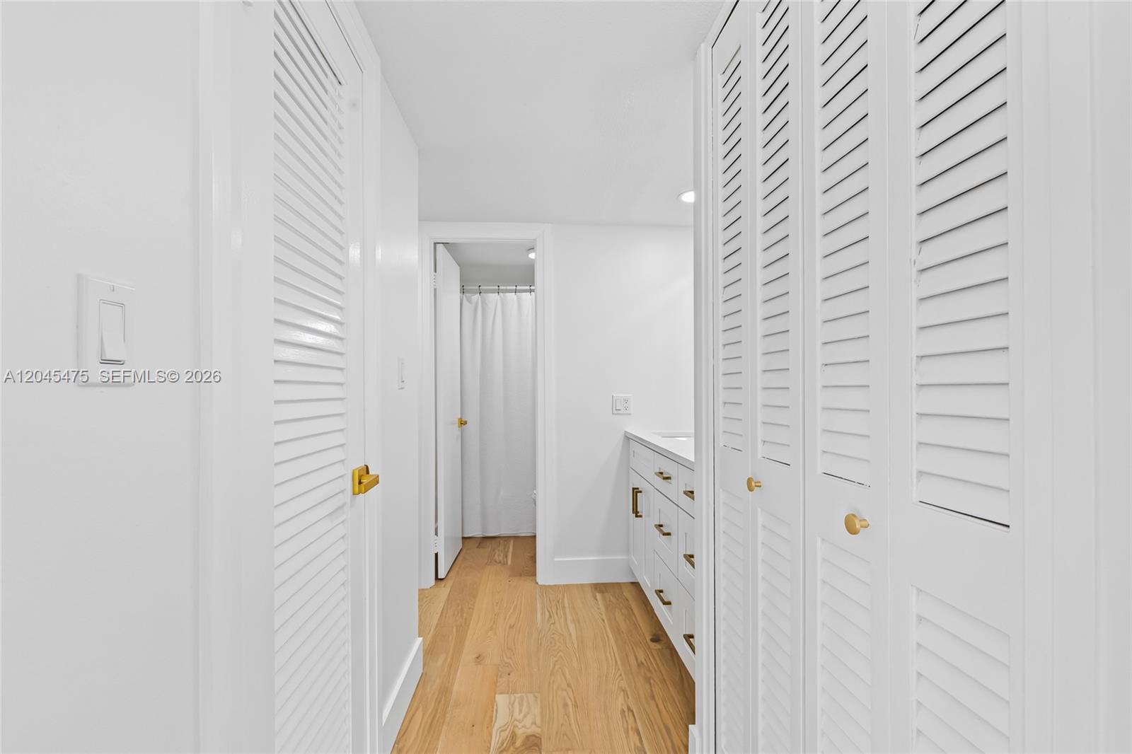 A hallway with light wood flooring leads to a bathroom featuring white cabinetry — 301 N Ocean Blvd # 302, Pompano Beach FL 33062, POMPANO BEACH, FL