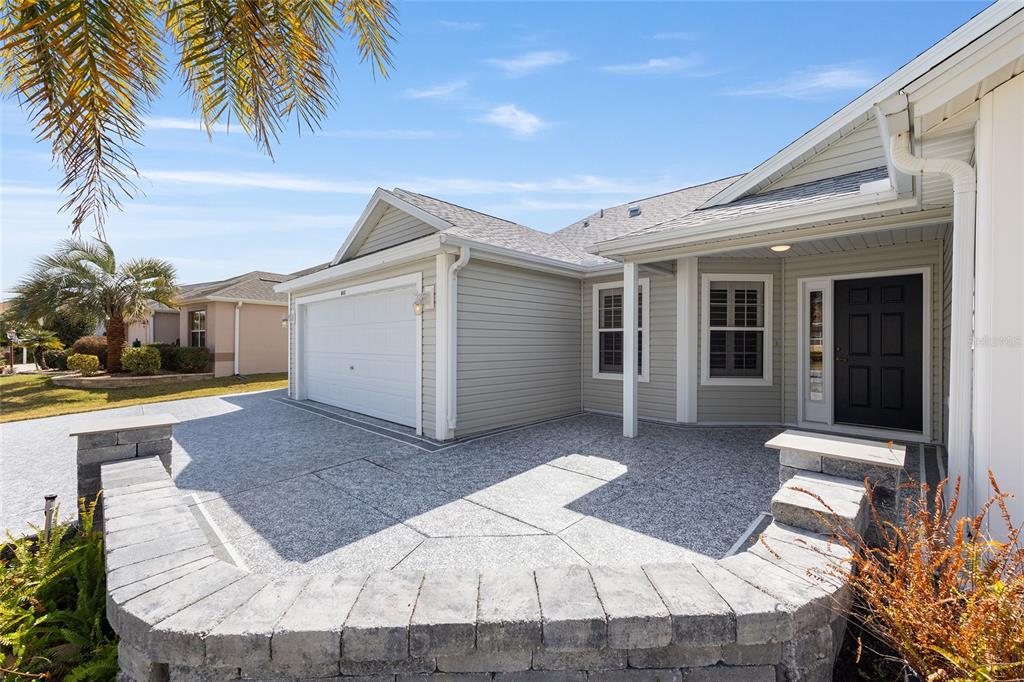 A light-colored house with a garage and a stone-walled patio in the front yard — 840 FOLSUM PLACE, THE VILLAGES, FL
