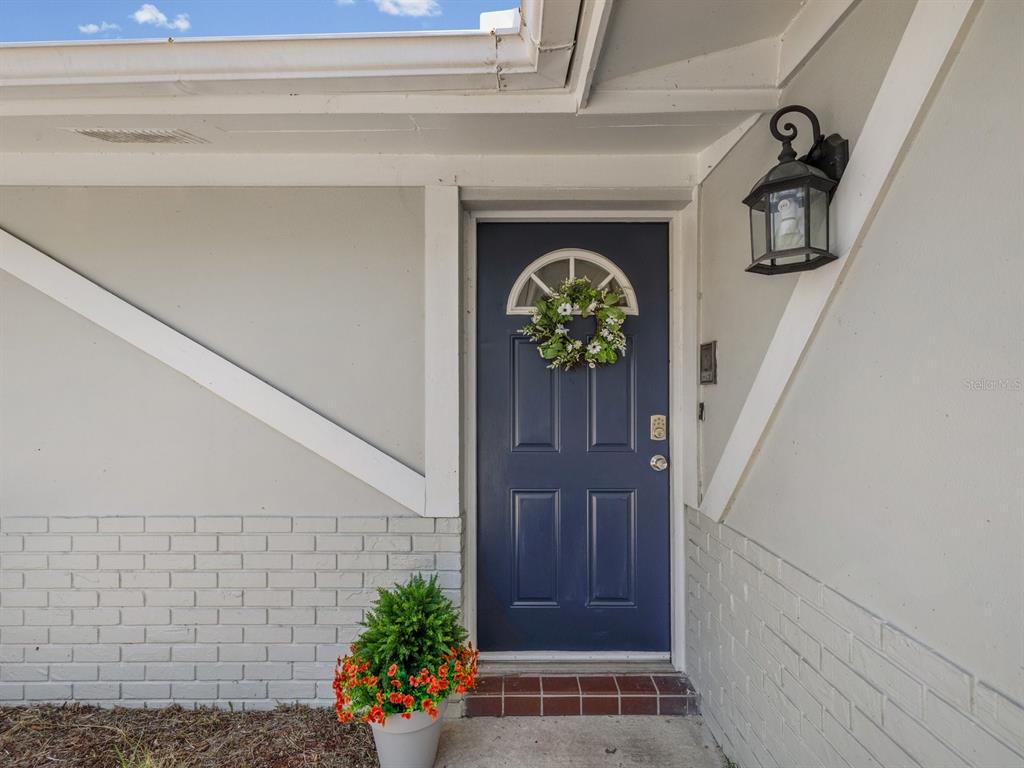 A dark blue front door with a wreath sits under a porch light — 9414 LEDGESTONE LANE, PORT RICHEY, FL