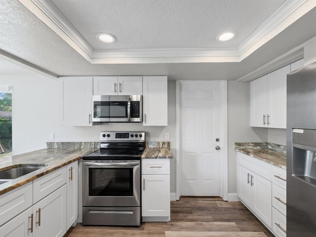 A kitchen features white cabinets, stainless steel appliances, and granite countertops with wood-look flooring — 9414 LEDGESTONE LANE, PORT RICHEY, FL