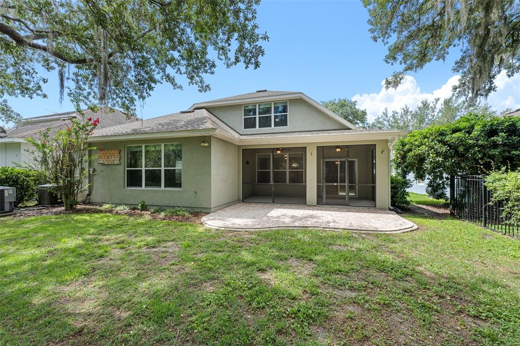 The back of a house features a screened-in patio, a paver terrace, and a lawn — 15814 STARLING WATER DRIVE, LITHIA, FL