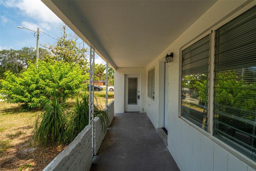 A covered concrete porch features white walls, a metal railing, and two exterior doors — 7204 ASTOR DRIVE, NEW PORT RICHEY, FL