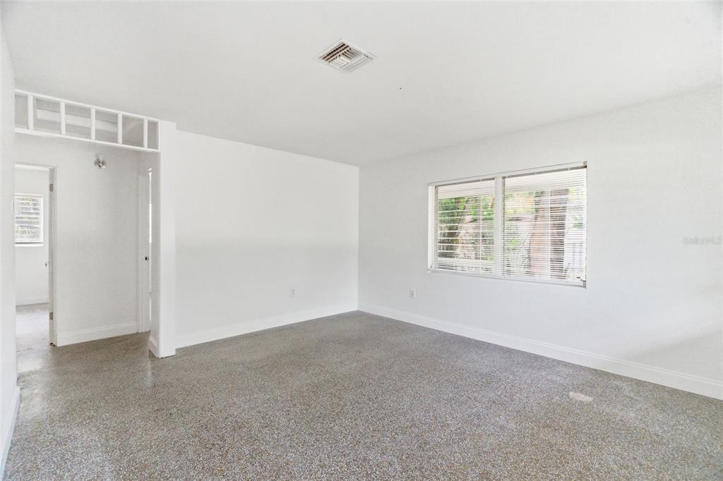 An empty room with white walls, a window with blinds, and speckled gray flooring — 7204 ASTOR DRIVE, NEW PORT RICHEY, FL