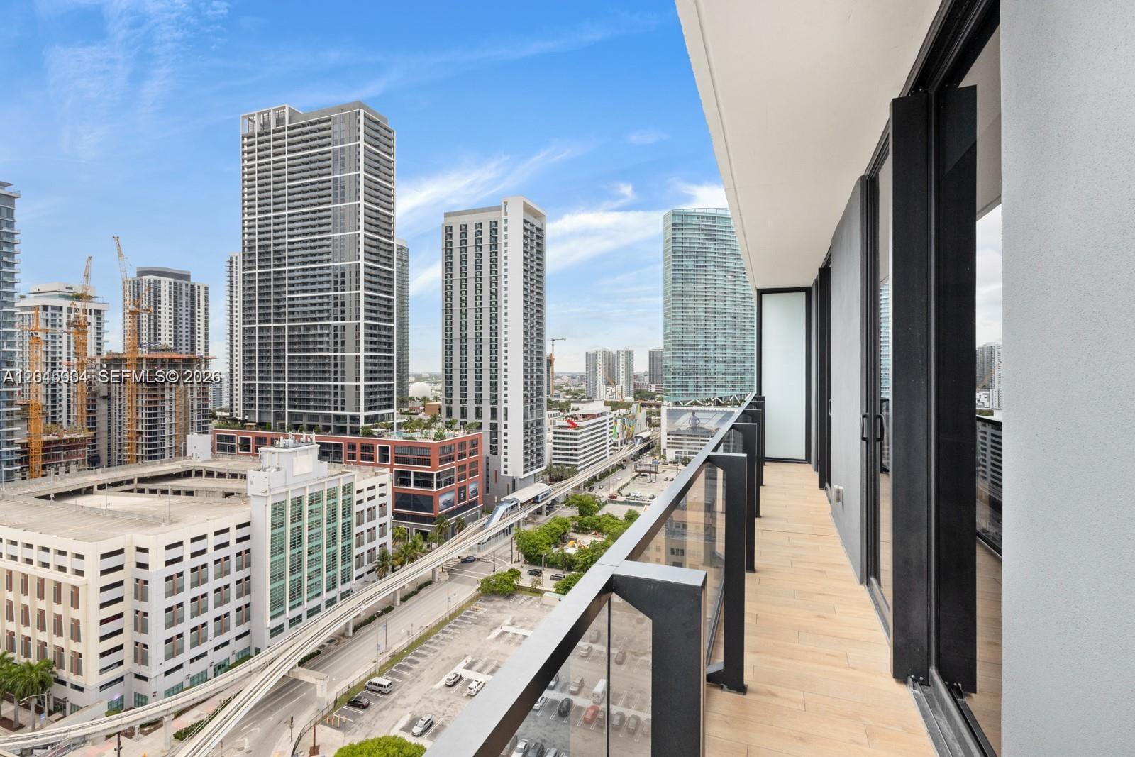 A high-rise balcony with wood-look tile flooring overlooks a city skyline and train tracks — 398 NE 5th St # 1518, Miami FL 33132, MIAMI, FL