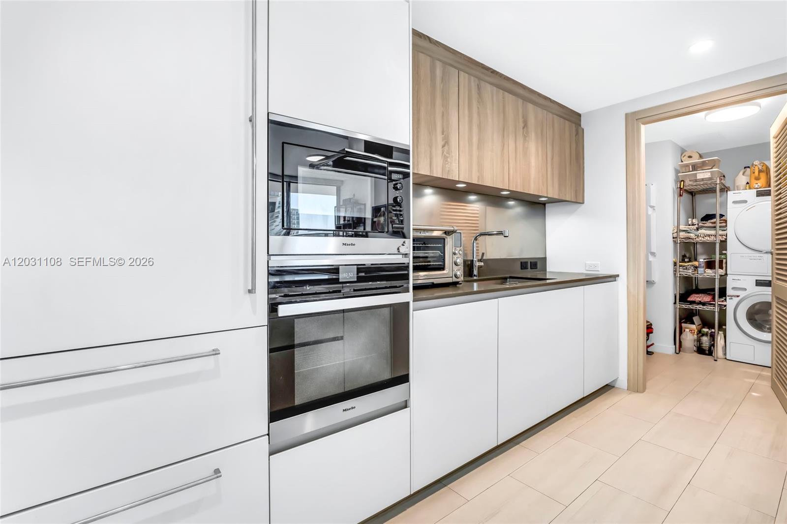 A modern kitchen features white cabinetry, stainless steel appliances, and an adjacent laundry area — 1000 Brickell Plz # 4609, Miami FL 33131, MIAMI, FL