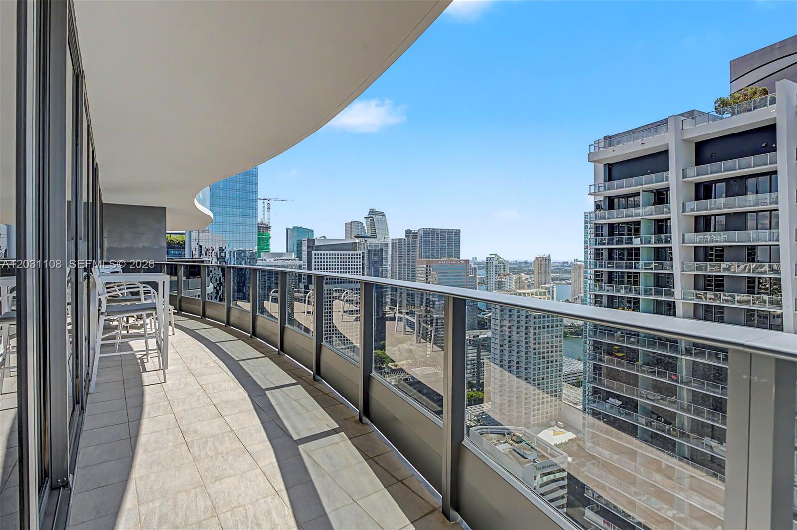 A high-rise balcony with tile flooring, glass railings, and outdoor seating overlooking a city skyline — 1000 Brickell Plz # 4609, Miami FL 33131, MIAMI, FL