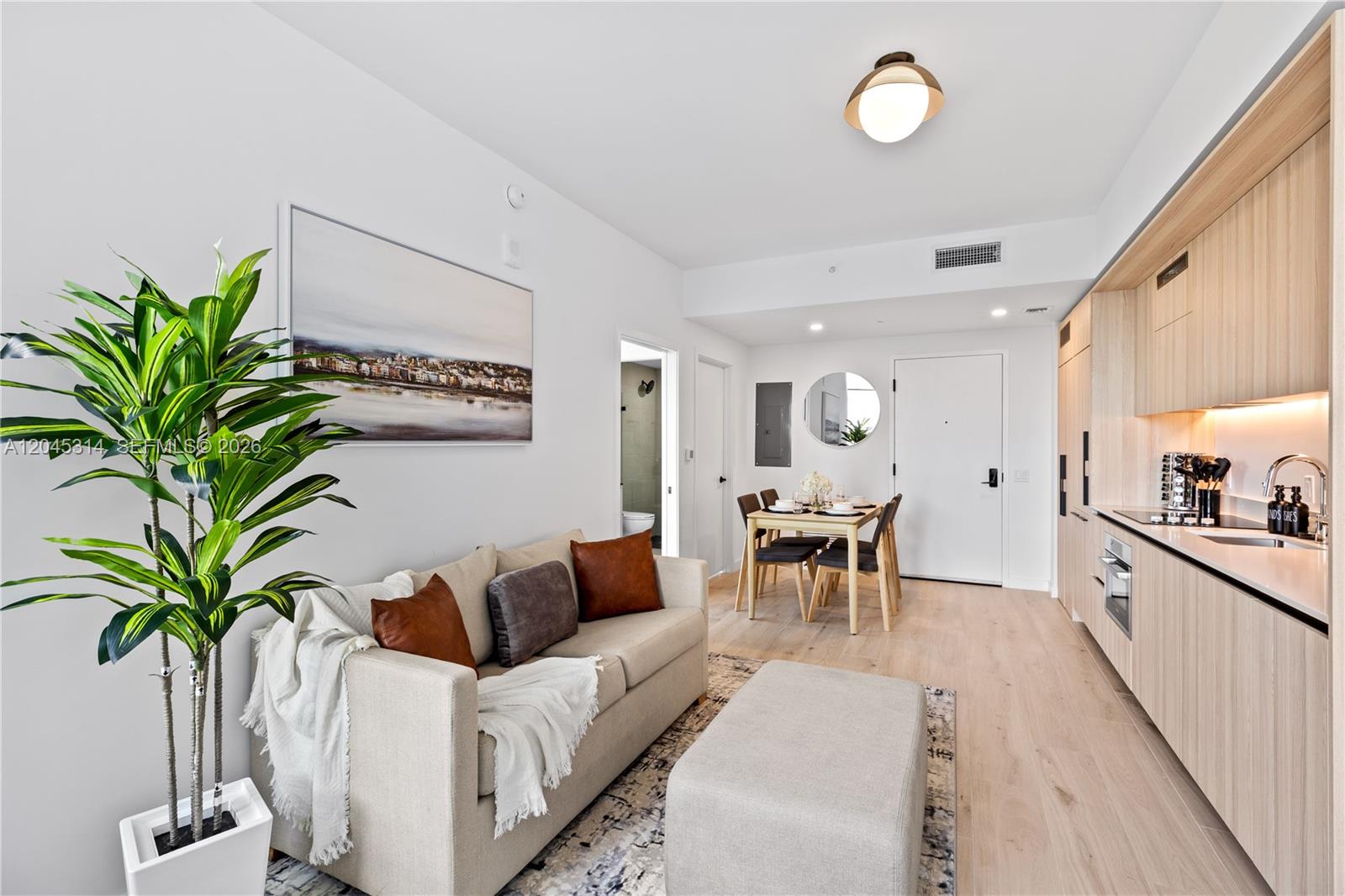A modern studio apartment features a sofa, dining area, and kitchen with light wood cabinetry — 225 N Miami Ave # 1102, Miami FL 33128, MIAMI, FL