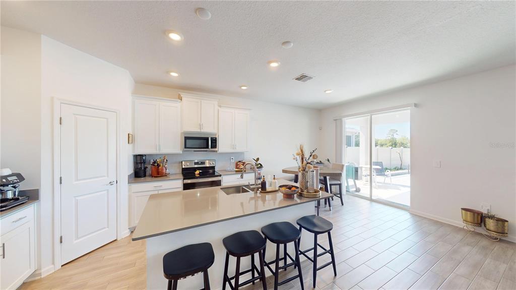 A kitchen with white cabinets, a central island with bar stools, and a sliding glass door — 6242 LAKEPINE STREET, ST CLOUD, FL