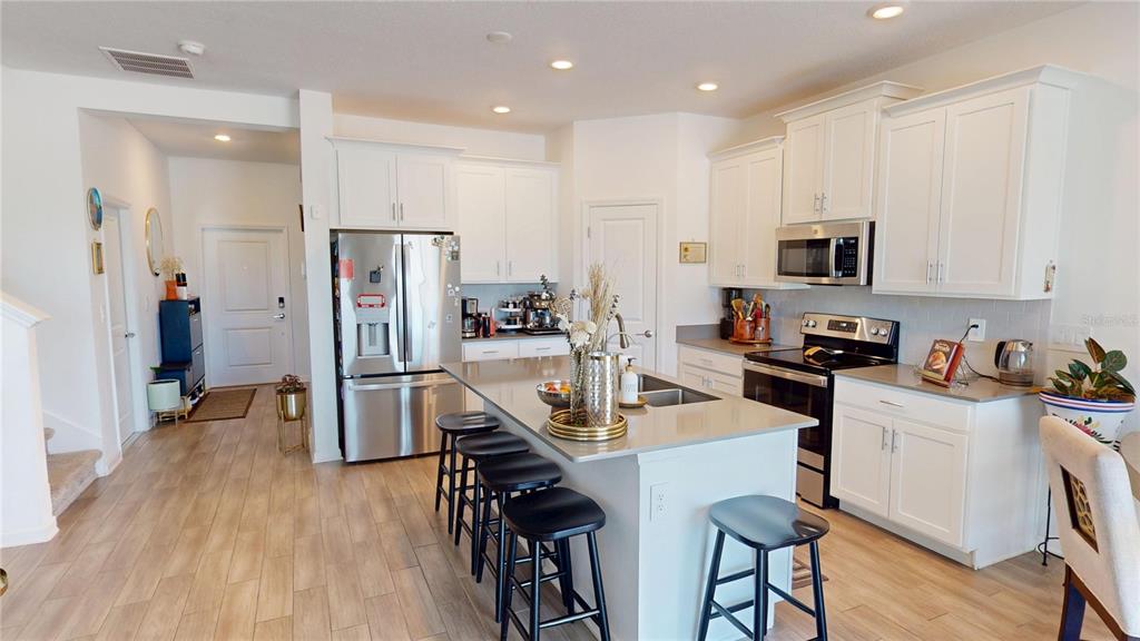 A modern kitchen features white cabinets, stainless steel appliances, a center island, and wood-look flooring — 6242 LAKEPINE STREET, ST CLOUD, FL