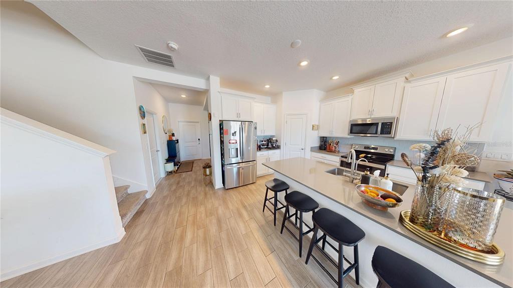 A modern kitchen features white cabinetry, stainless steel appliances, a quartz island, and wood-look flooring — 6242 LAKEPINE STREET, ST CLOUD, FL