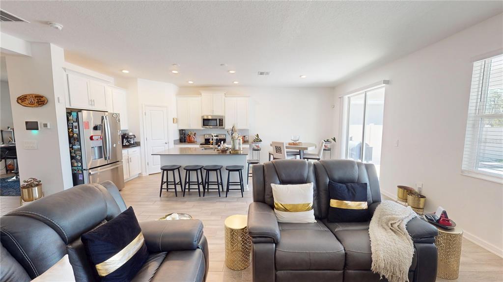 An open-concept kitchen and living area features white cabinetry, a central island, and gray furniture — 6242 LAKEPINE STREET, ST CLOUD, FL