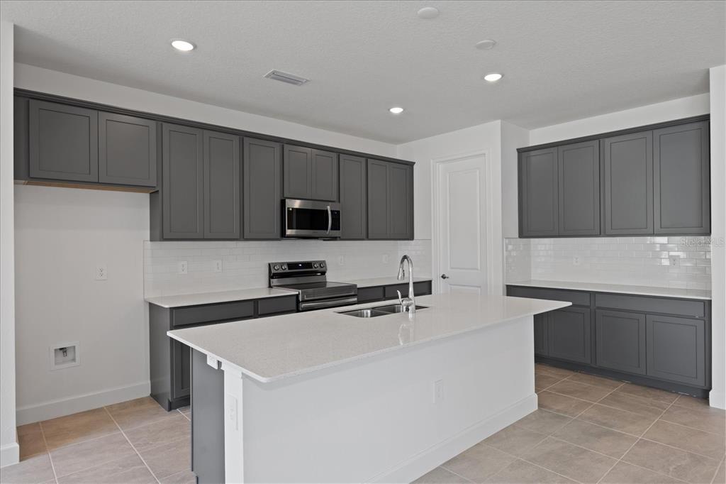 A kitchen features gray cabinets, white countertops, a central island, and a tile backsplash — 9593 VIBRANT LANE, VENICE, FL