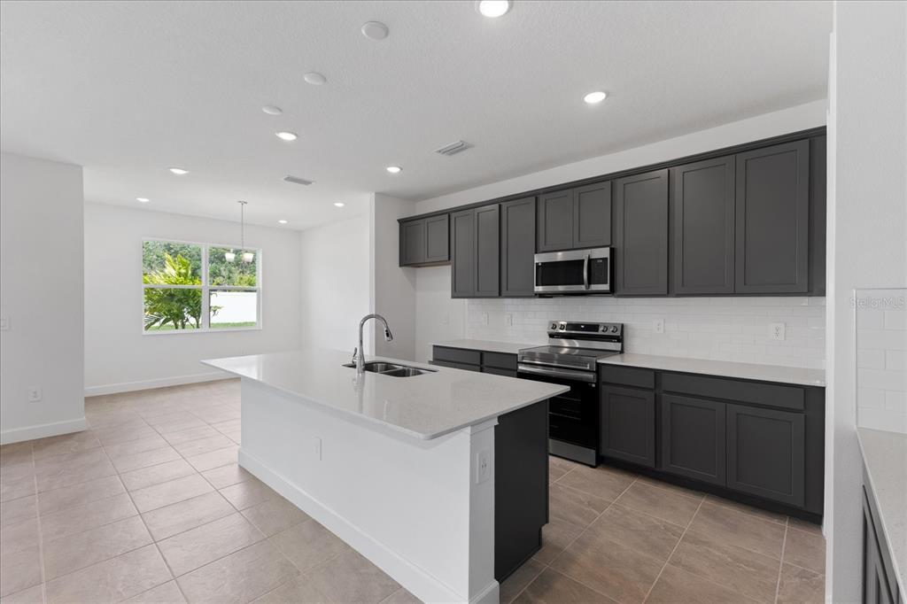 A modern kitchen features dark gray cabinets, white countertops, a central island, and tile flooring — 9593 VIBRANT LANE, VENICE, FL