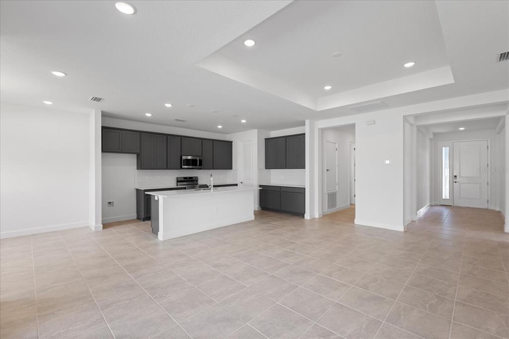 A modern kitchen features dark gray cabinetry, a white island, and light tile flooring — 9593 VIBRANT LANE, VENICE, FL