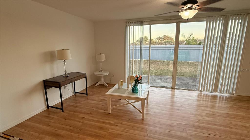 A living room with light wood flooring, a coffee table, a desk, and sliding glass doors — 227 ORCHID DRIVE, DAVENPORT, FL