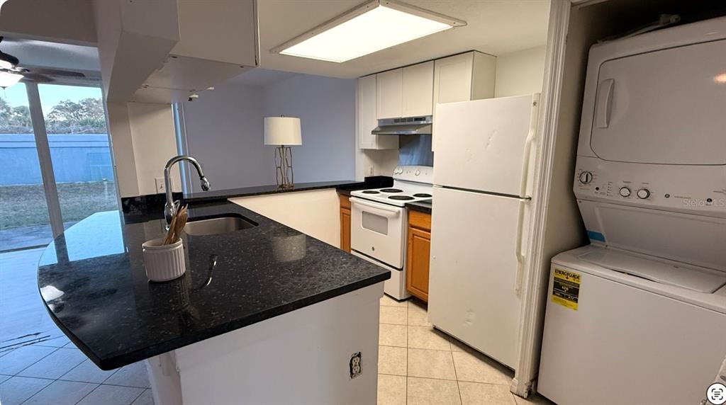 A kitchen features dark granite countertops, white cabinets, white appliances, and a stacked laundry unit — 227 ORCHID DRIVE, DAVENPORT, FL