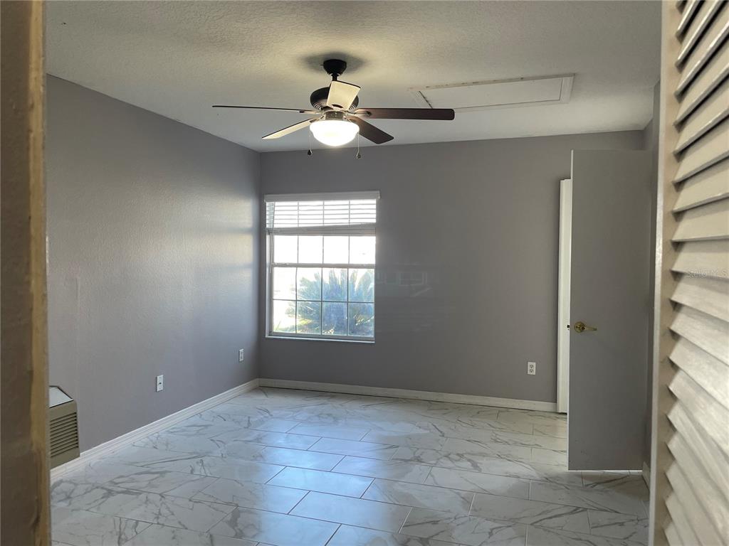 A bedroom with gray walls, white marble-look tile flooring, a ceiling fan, and a window — 227 ORCHID DRIVE, DAVENPORT, FL