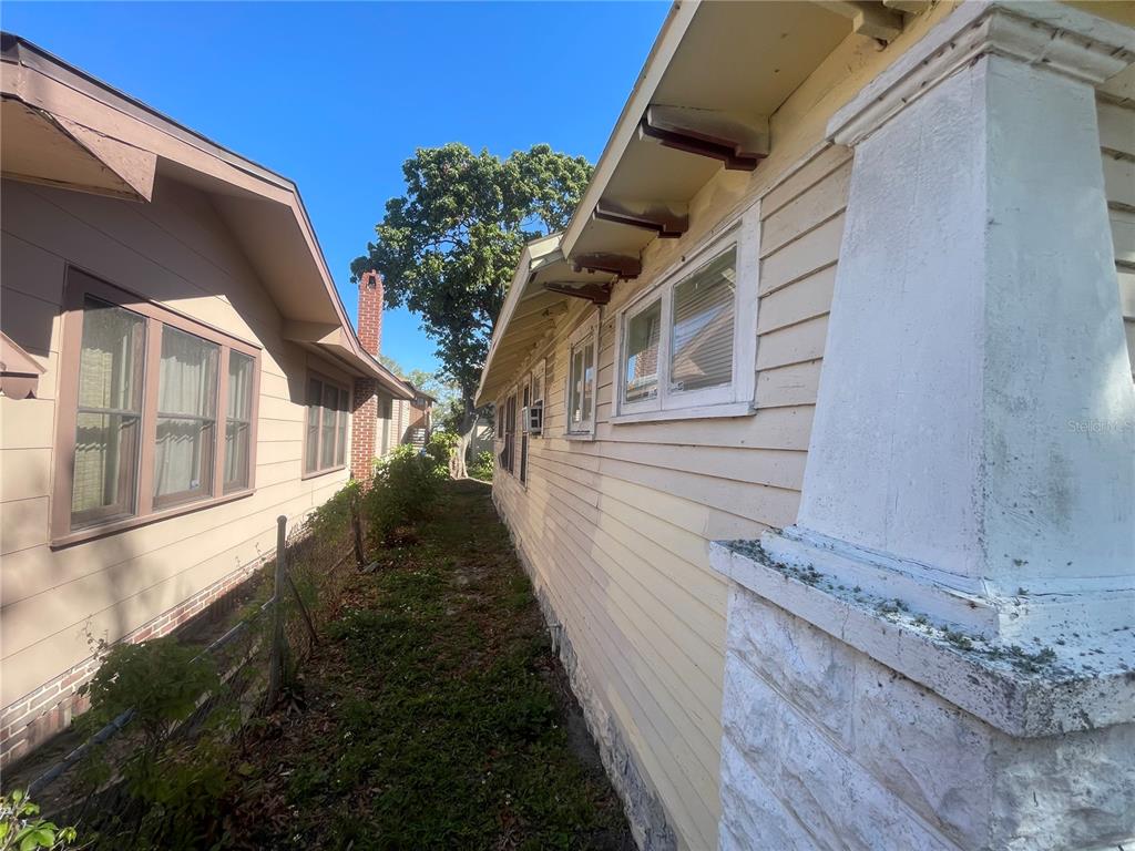 A narrow outdoor walkway between two light-colored houses with wood siding and a brick chimney — 1511 19TH AVENUE S, ST PETERSBURG, FL
