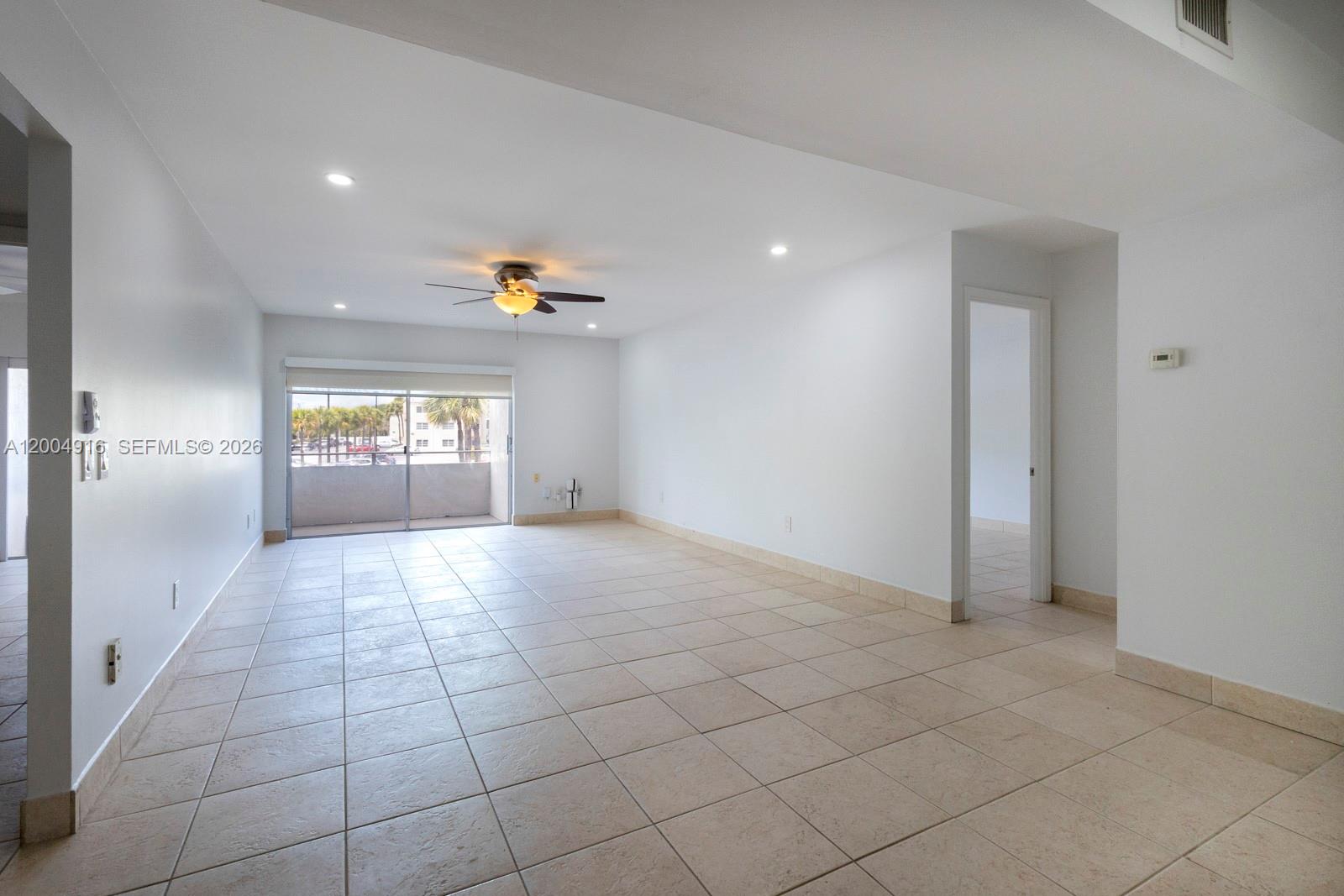 An empty living room features white walls, light-colored tile flooring, a ceiling fan, and a balcony — 7747 SW 86th St # 205, Miami FL 33143, MIAMI, FL