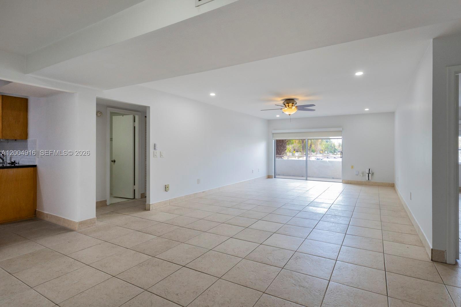 An empty living area features white walls, beige tile flooring, a ceiling fan, and a balcony — 7747 SW 86th St # 205, Miami FL 33143, MIAMI, FL