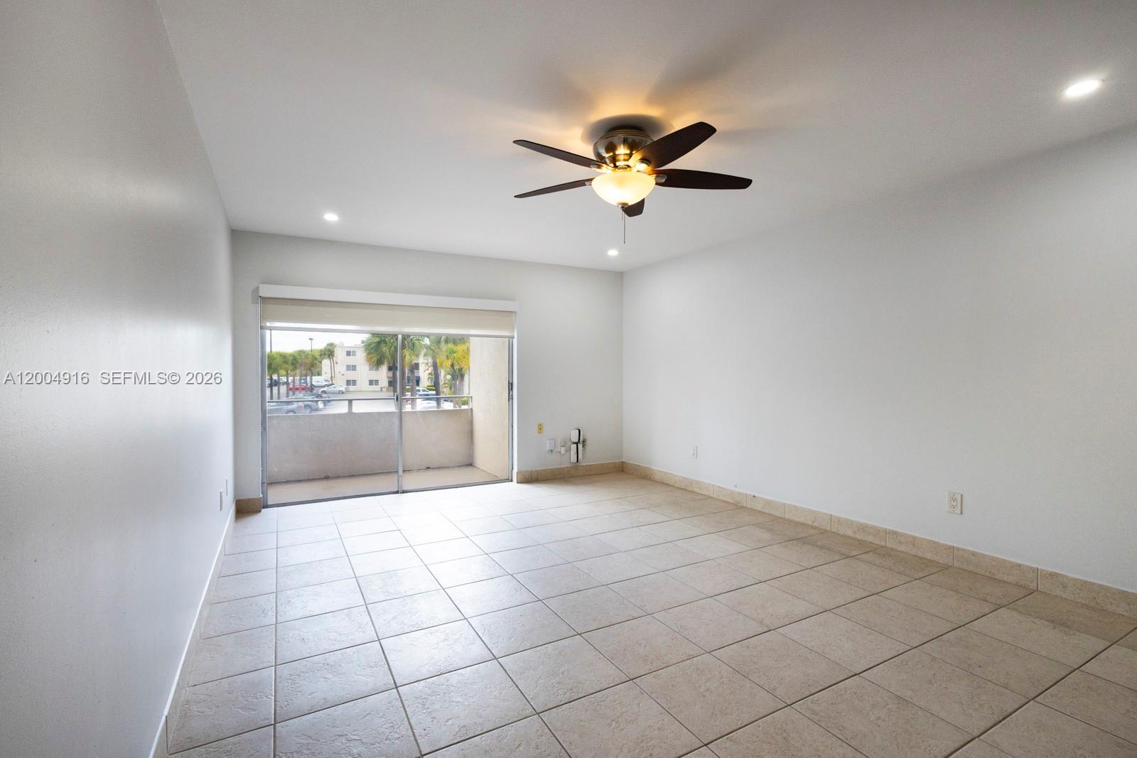 An empty room features light-colored tile flooring, a ceiling fan, and a sliding glass door — 7747 SW 86th St # 205, Miami FL 33143, MIAMI, FL