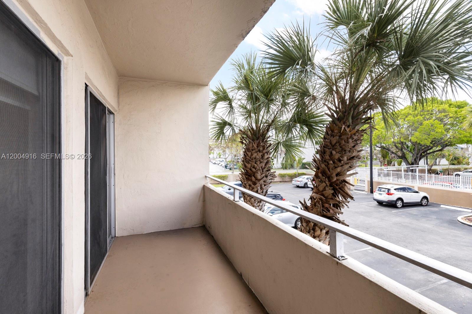 A covered balcony overlooks a parking lot with palm trees and several parked cars — 7747 SW 86th St # 205, Miami FL 33143, MIAMI, FL
