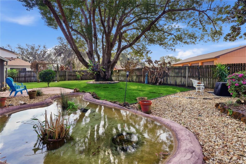 A backyard features a small pond, a large tree, a green lawn, and a wooden fence — 1307 ORTEGA STREET, WINTER SPRINGS, FL
