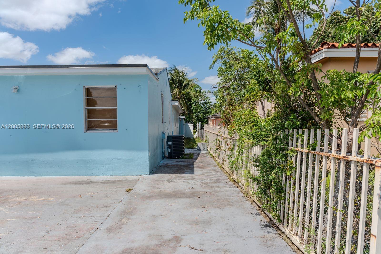 A concrete driveway runs alongside a light blue house with a metal fence — 141 E 16th St, Hialeah FL 33010, HIALEAH, FL