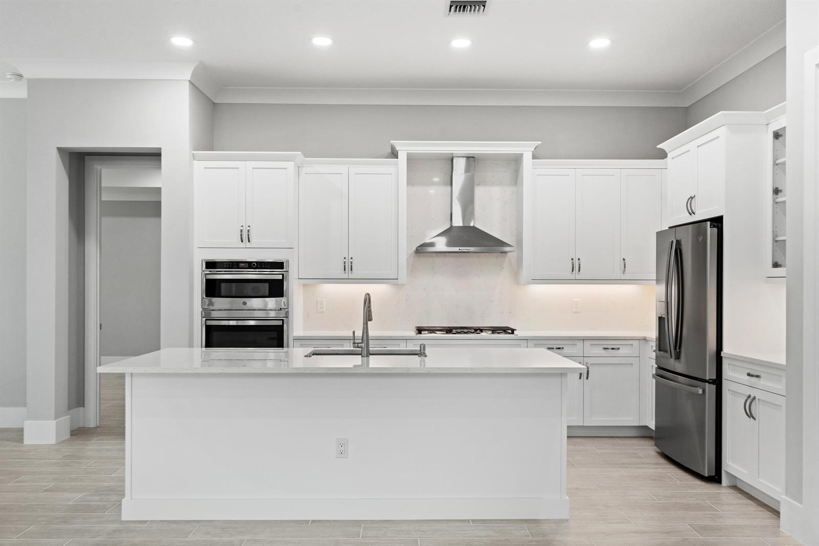 A modern kitchen features white cabinetry, a central island, stainless steel appliances, and light flooring — 692 Ravens Landing Drive, Vero Beach FL 32968, VERO BEACH, FL