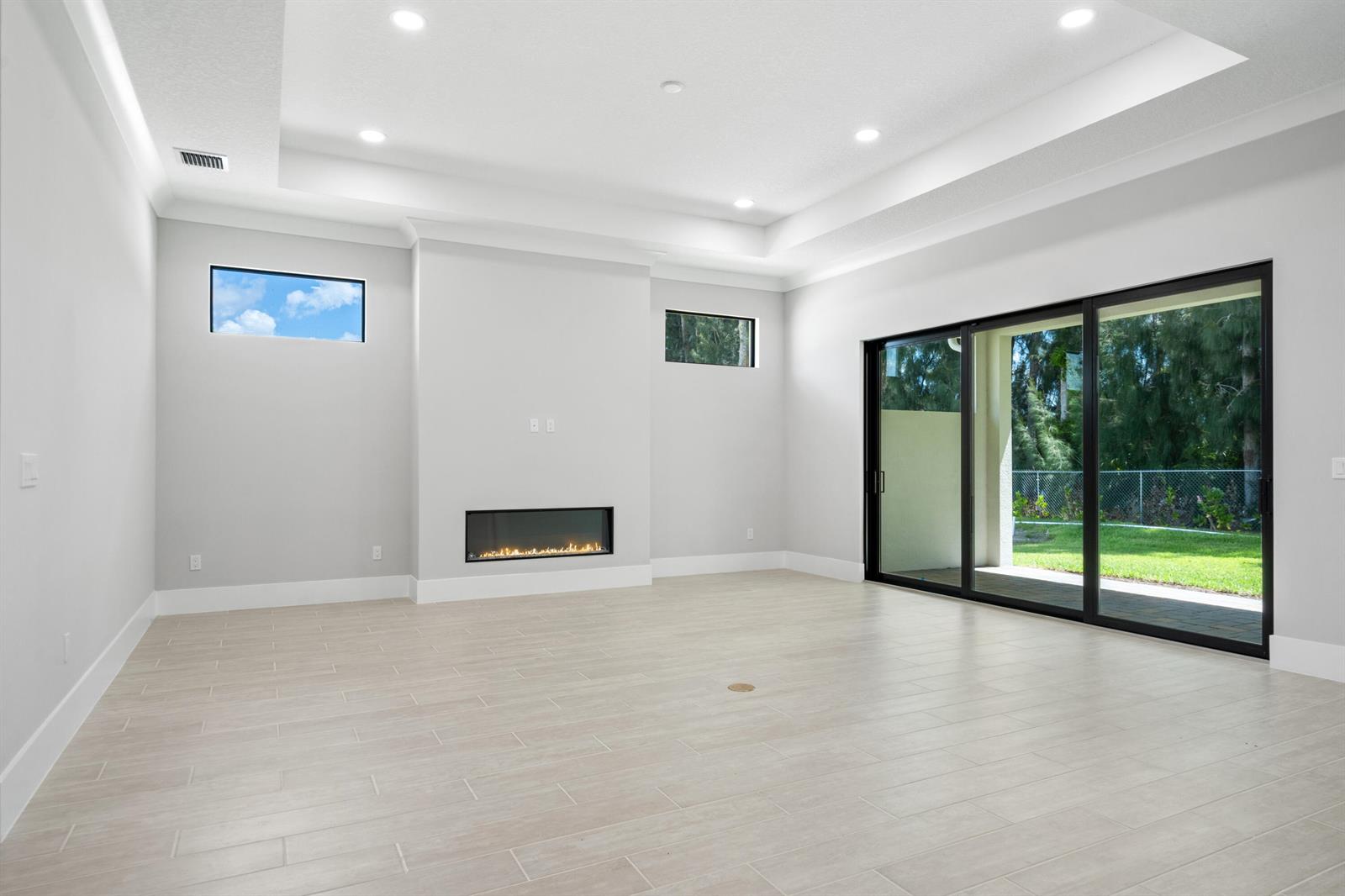 A modern living room features a linear fireplace, tray ceiling, and large sliding glass doors — 692 Ravens Landing Drive, Vero Beach FL 32968, VERO BEACH, FL