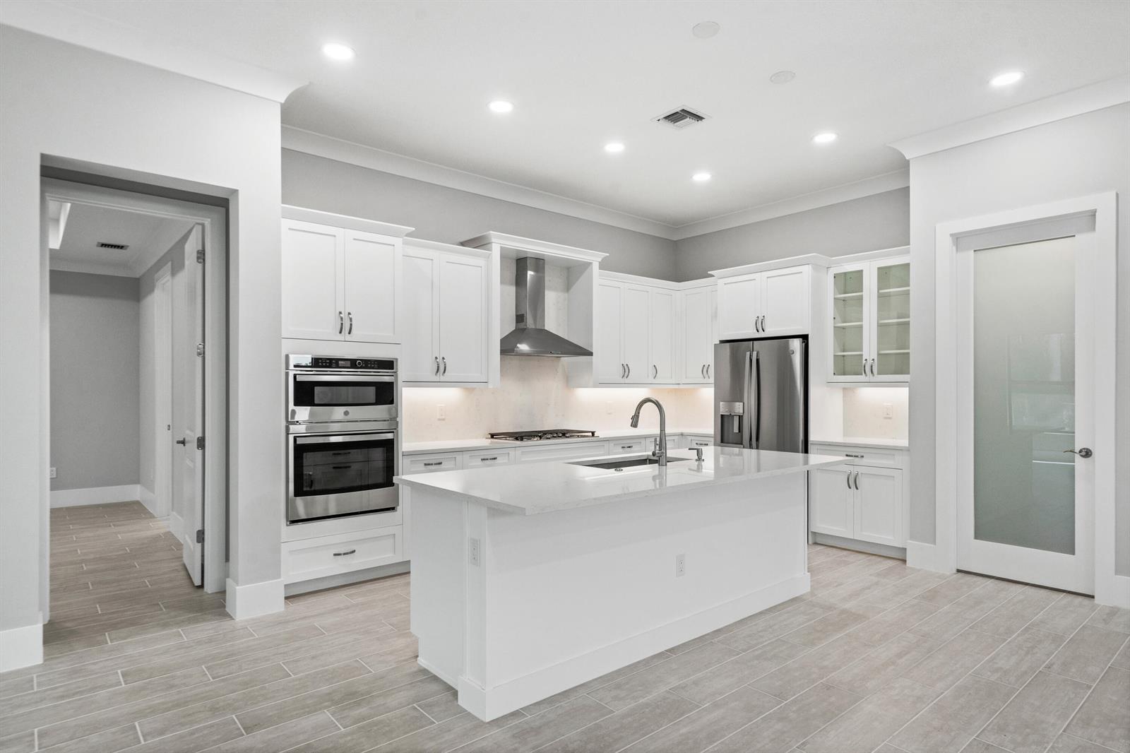 A modern kitchen features white cabinetry, stainless steel appliances, a central island, and tile flooring — 692 Ravens Landing Drive, Vero Beach FL 32968, VERO BEACH, FL