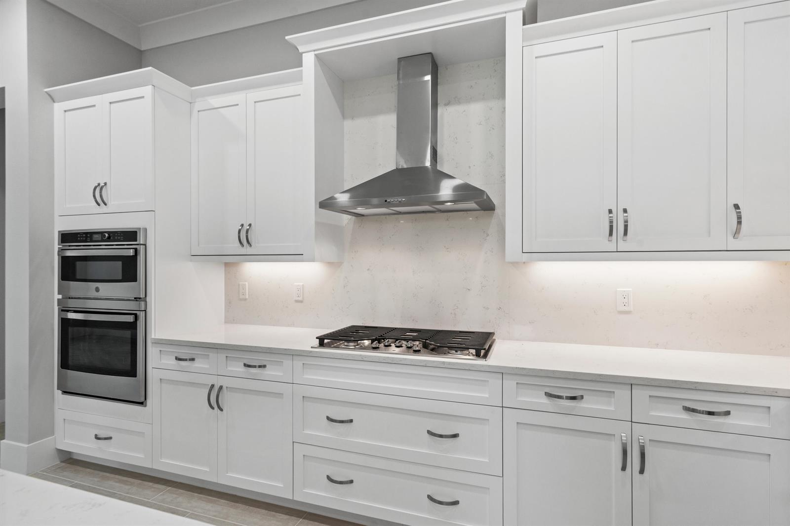 A modern kitchen features white cabinets, stainless steel appliances, a gas cooktop, and quartz countertops — 692 Ravens Landing Drive, Vero Beach FL 32968, VERO BEACH, FL