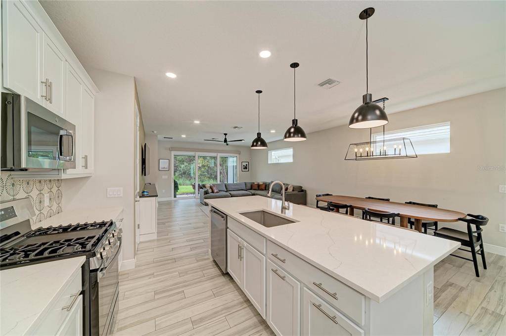 A modern kitchen features white cabinets, a quartz island, and a dining area with pendant lights — 1079 WATERLINE COURT, SARASOTA, FL