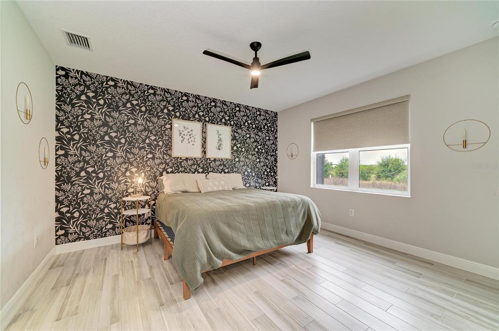A bedroom features a black and white floral accent wall, light wood flooring, and a bed — 1079 WATERLINE COURT, SARASOTA, FL