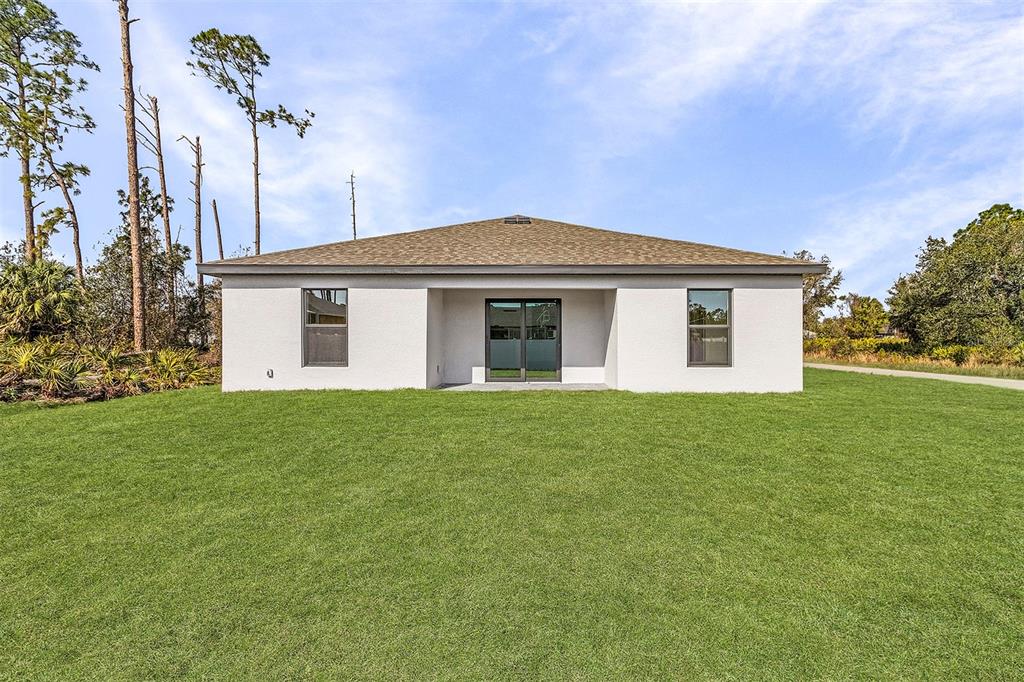 The exterior rear view of a single-story house features a lawn and sliding glass doors — 5830 BABIAN ROAD, NORTH PORT, FL