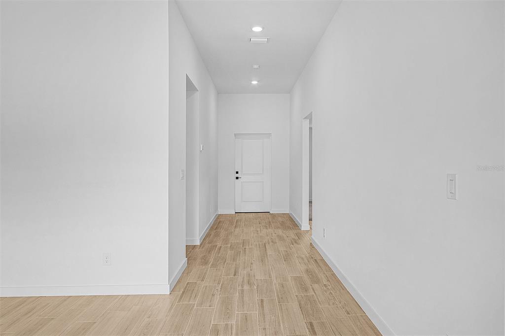 A bright hallway with light wood-look tile flooring leads to a white front door — 5830 BABIAN ROAD, NORTH PORT, FL