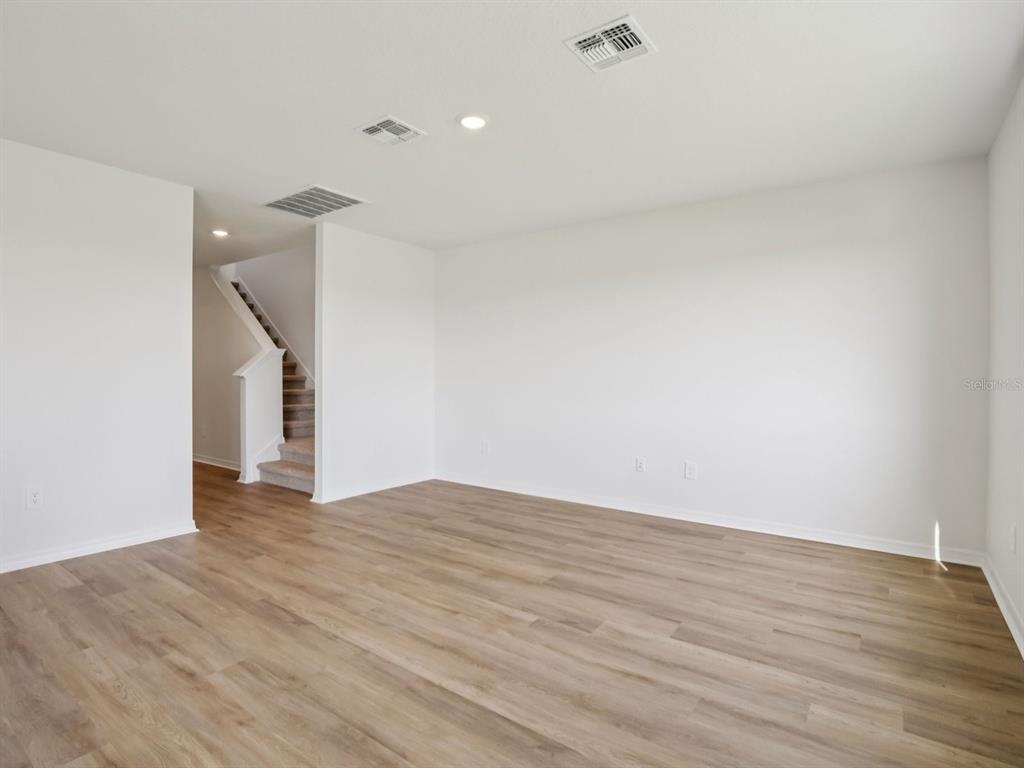 An empty room with light wood-look flooring, white walls, and a staircase in the background — 11316 BELLEWOOD TERRACE, PARRISH, FL